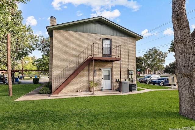 back of property with a yard, stairway, brick siding, central AC unit, and a chimney