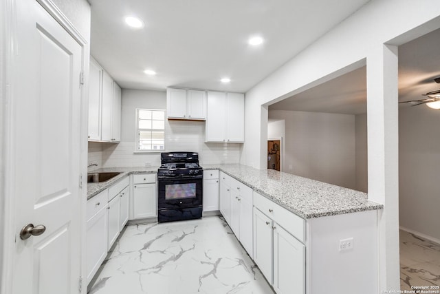 kitchen with marble finish floor, a sink, black gas range oven, white cabinets, and decorative backsplash