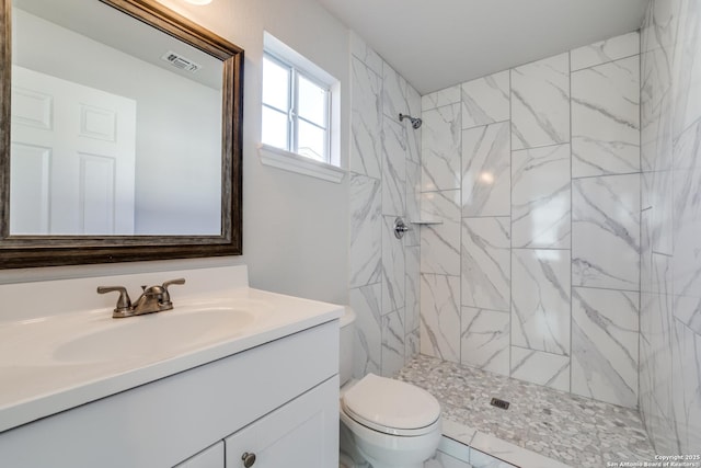 bathroom featuring visible vents, toilet, marble finish floor, tiled shower, and vanity