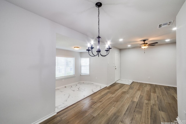 unfurnished dining area featuring visible vents, baseboards, wood finished floors, and ceiling fan with notable chandelier