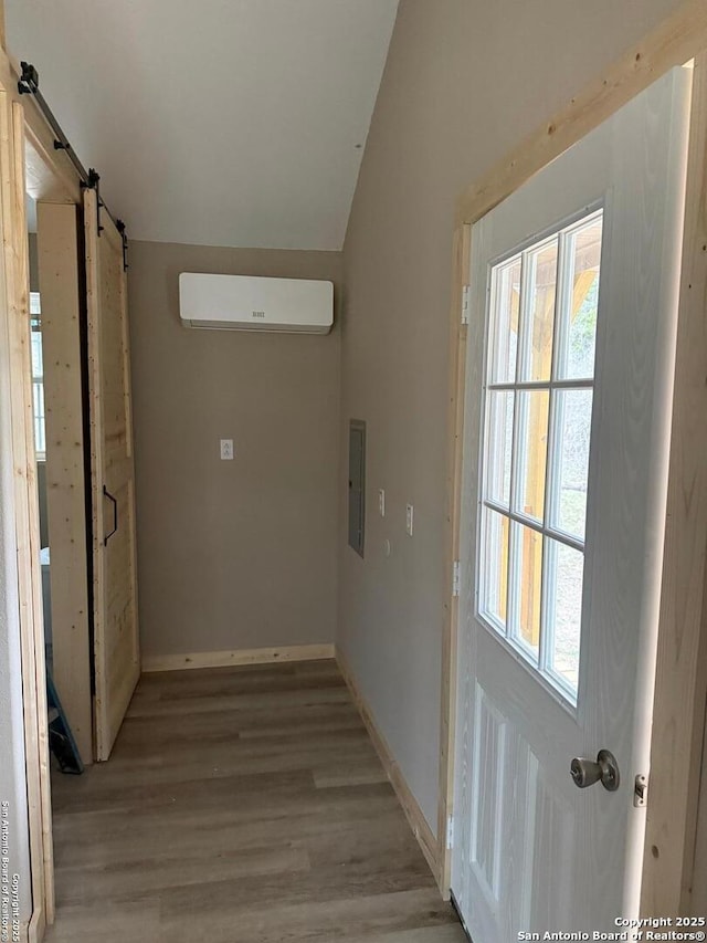 hall with lofted ceiling, light wood-style flooring, electric panel, a wall mounted air conditioner, and a barn door