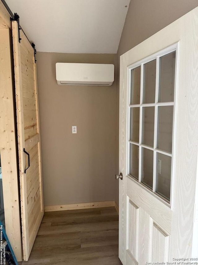 interior space featuring baseboards, a barn door, lofted ceiling, wood finished floors, and a wall mounted AC