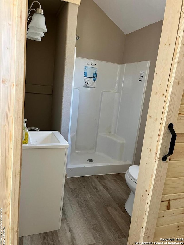 full bathroom featuring toilet, a stall shower, wood finished floors, lofted ceiling, and vanity