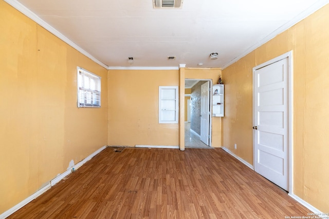 spare room with baseboards, wood finished floors, visible vents, and ornamental molding