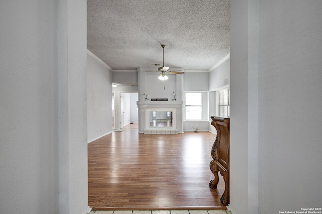 living area with light wood finished floors, a textured ceiling, a tiled fireplace, crown molding, and a textured wall