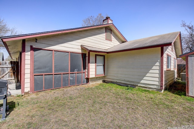 rear view of property featuring fence, central AC, a chimney, a yard, and a sunroom