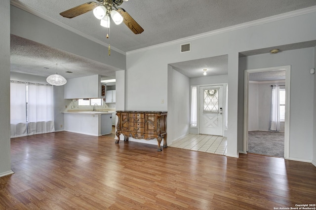 living area with visible vents, a textured ceiling, crown molding, and wood finished floors