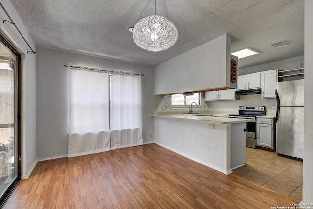 kitchen with under cabinet range hood, light countertops, a peninsula, stainless steel appliances, and a sink