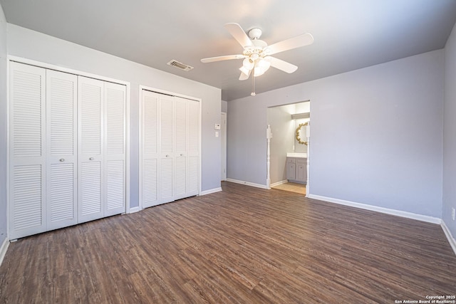 unfurnished bedroom with visible vents, baseboards, multiple closets, and dark wood-style flooring