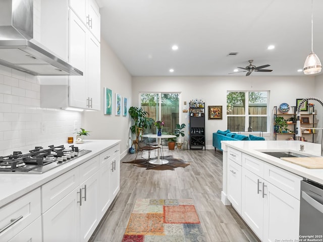 kitchen with visible vents, wall chimney range hood, light countertops, stainless steel appliances, and a sink