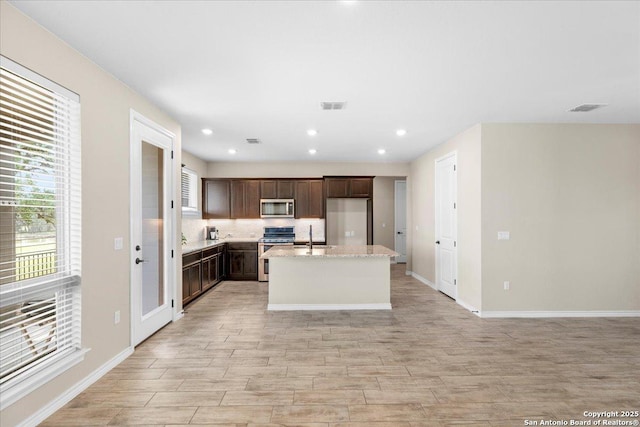 kitchen with visible vents, a kitchen island with sink, dark brown cabinetry, appliances with stainless steel finishes, and decorative backsplash