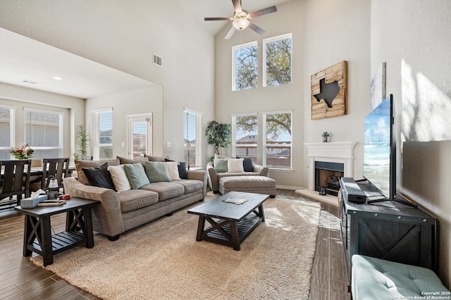 living area featuring ceiling fan, visible vents, a fireplace with raised hearth, and dark wood finished floors