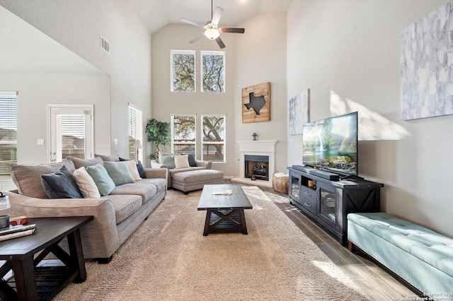 living room featuring visible vents, a fireplace with raised hearth, wood finished floors, high vaulted ceiling, and a ceiling fan