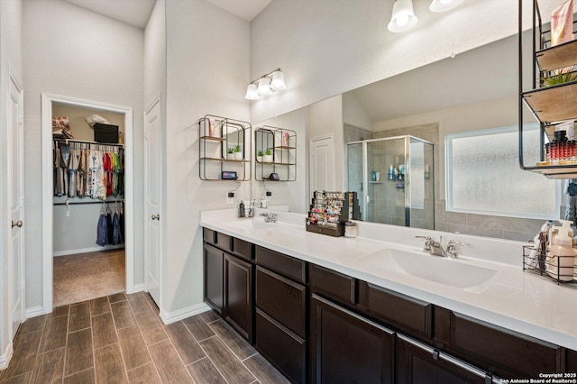 full bathroom featuring wood tiled floor, double vanity, a sink, a shower stall, and a walk in closet