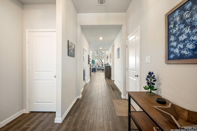 hall with visible vents, baseboards, and dark wood-style flooring