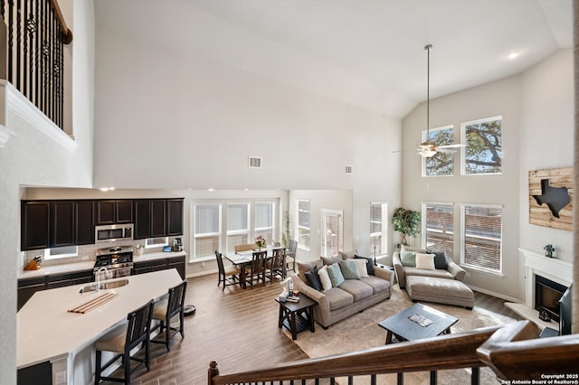 living area featuring visible vents, dark wood-type flooring, a ceiling fan, a glass covered fireplace, and vaulted ceiling