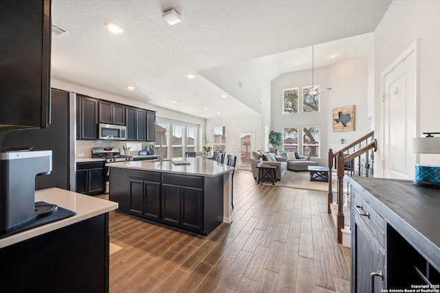 kitchen featuring an island with sink, dark wood-style floors, stainless steel appliances, light countertops, and decorative backsplash