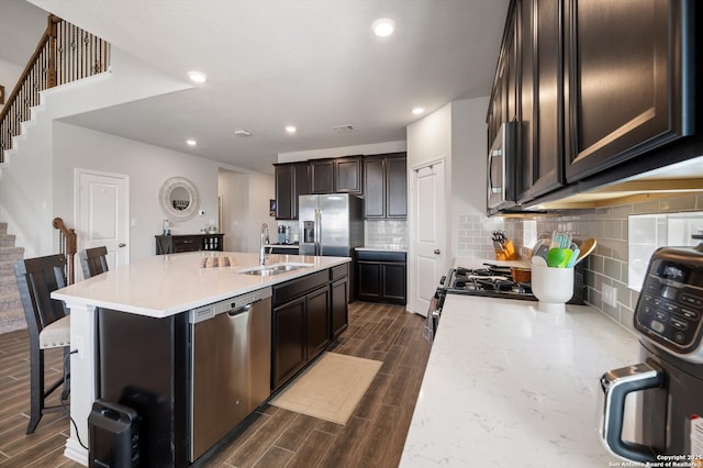 kitchen featuring wood finish floors, a sink, decorative backsplash, stainless steel appliances, and a kitchen breakfast bar