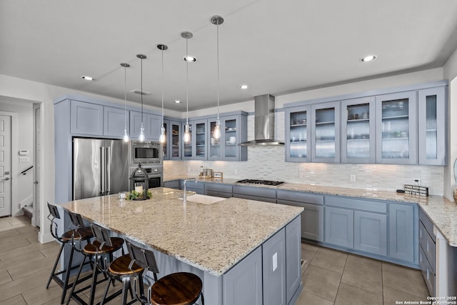 kitchen with backsplash, wall chimney range hood, a breakfast bar area, appliances with stainless steel finishes, and a sink