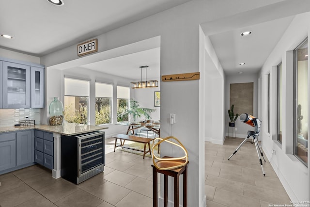 kitchen with backsplash, wine cooler, a peninsula, glass insert cabinets, and light stone countertops