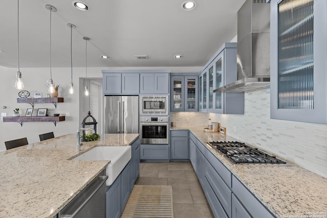 kitchen with light stone counters, recessed lighting, appliances with stainless steel finishes, wall chimney exhaust hood, and tasteful backsplash