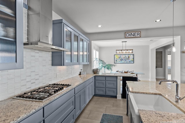 kitchen featuring a sink, stainless steel gas stovetop, wall chimney exhaust hood, light tile patterned floors, and hanging light fixtures