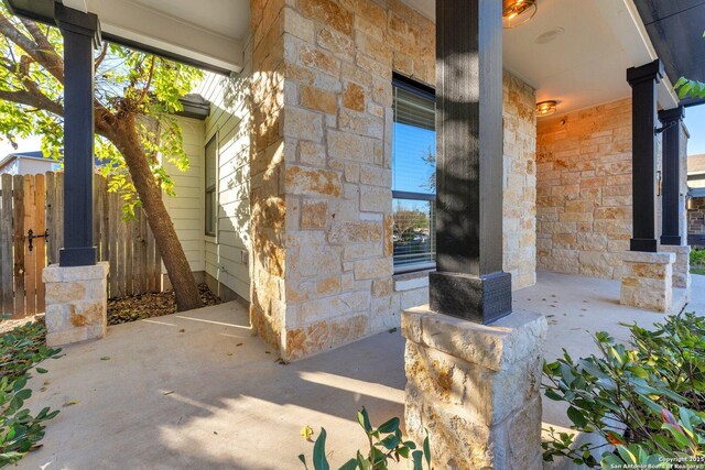 doorway to property featuring a porch, fence, and stone siding