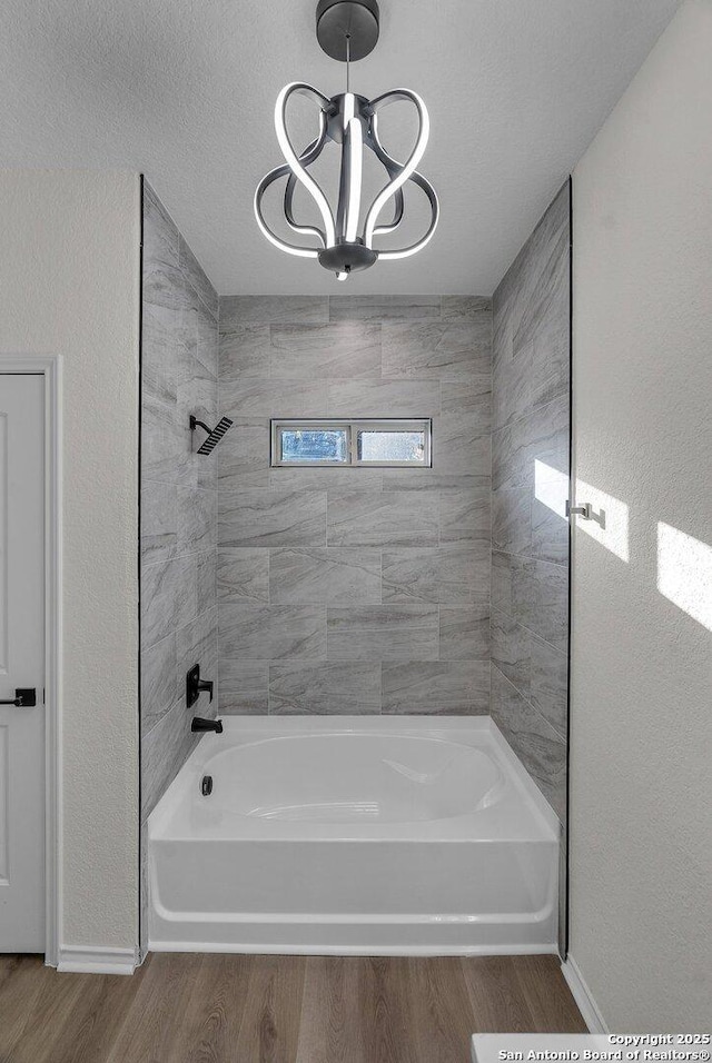 full bathroom with washtub / shower combination, wood finished floors, baseboards, a textured ceiling, and a chandelier