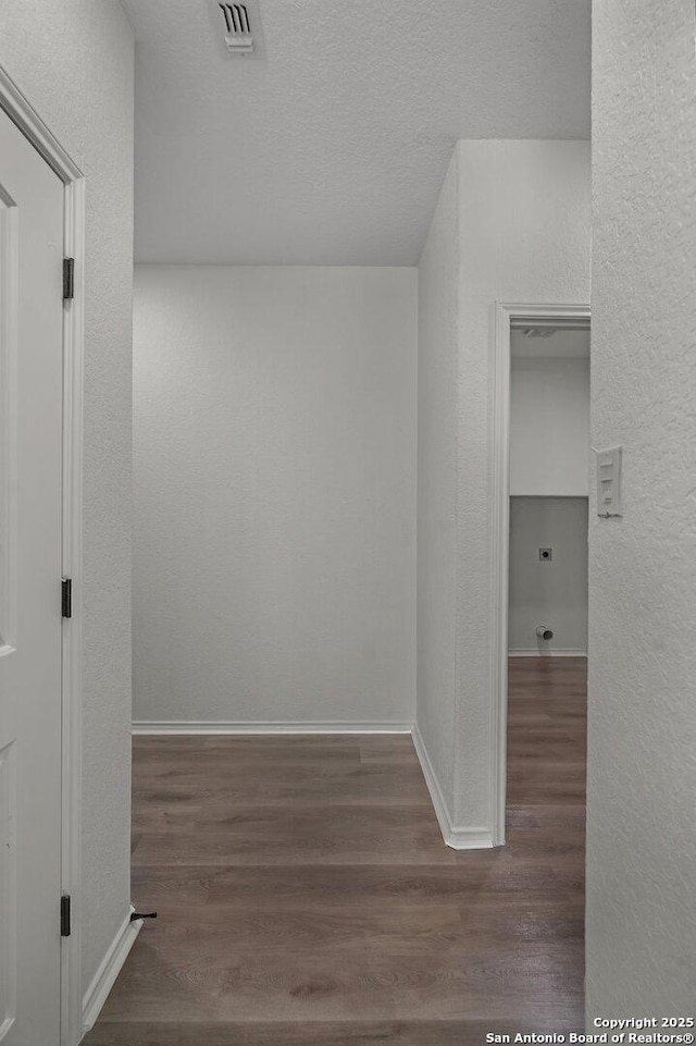 corridor featuring wood finished floors, visible vents, a textured wall, and a textured ceiling