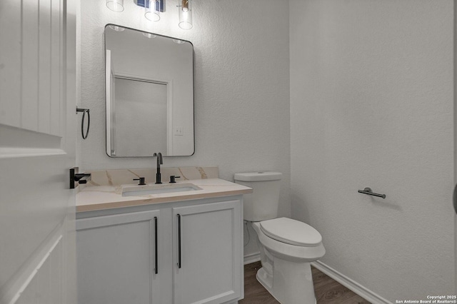 bathroom with vanity, wood finished floors, baseboards, toilet, and a textured wall