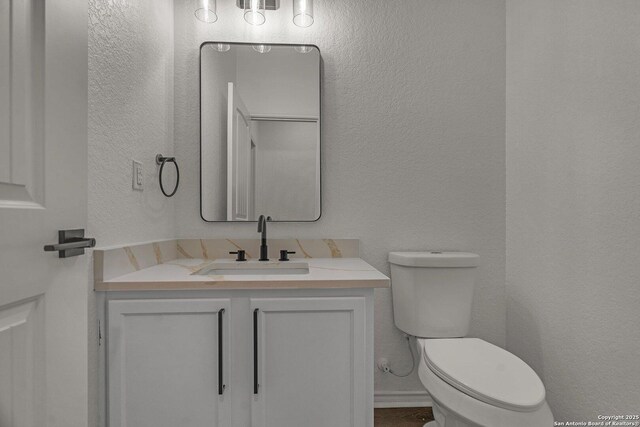 bathroom with vanity, toilet, and a textured wall