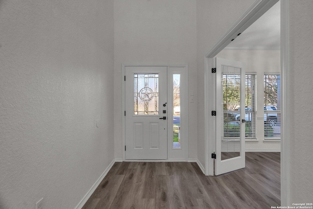 foyer entrance with ornamental molding, baseboards, a textured wall, and wood finished floors