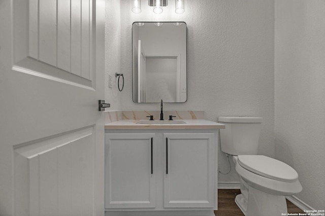 half bathroom with vanity, toilet, wood finished floors, and a textured wall