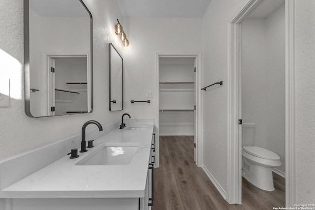 bathroom with a spacious closet, toilet, wood finished floors, and a sink