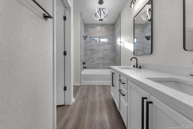 full bath with a sink, wood finished floors, double vanity, shower / bathtub combination, and a textured wall