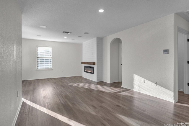 unfurnished living room featuring wood finished floors, a fireplace, visible vents, and baseboards