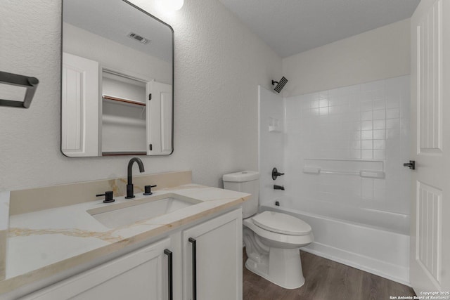 full bathroom featuring vanity, wood finished floors, visible vents, toilet, and a textured wall