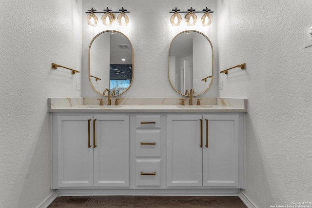 full bath featuring double vanity, a textured wall, and a sink