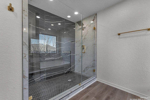 full bath featuring a textured wall, wood finished floors, baseboards, and a marble finish shower