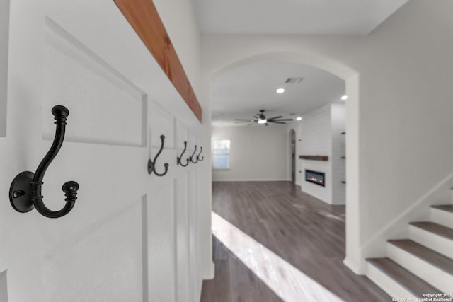 interior space with wood finished floors, a fireplace, arched walkways, ceiling fan, and stairs