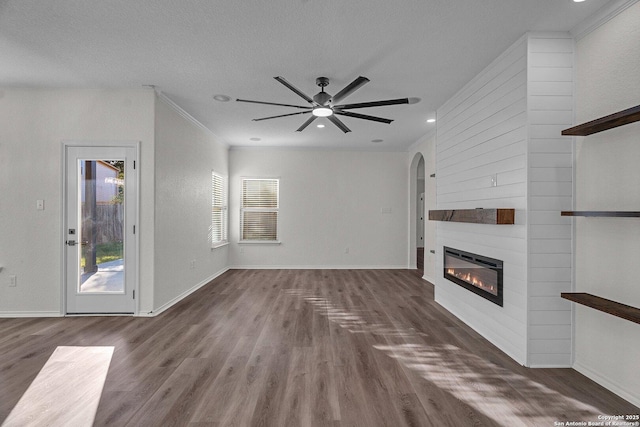 unfurnished living room featuring crown molding, a large fireplace, a ceiling fan, and wood finished floors