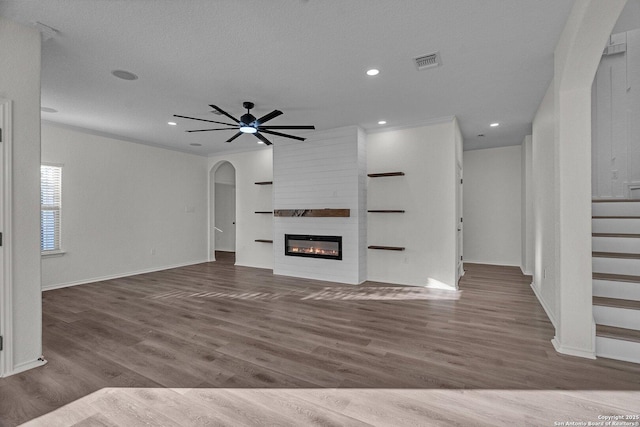 unfurnished living room with stairway, wood finished floors, visible vents, a fireplace, and arched walkways