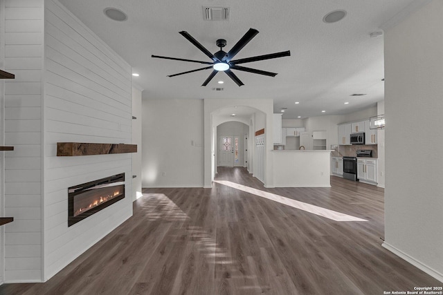 unfurnished living room with dark wood-style floors, visible vents, recessed lighting, arched walkways, and a large fireplace