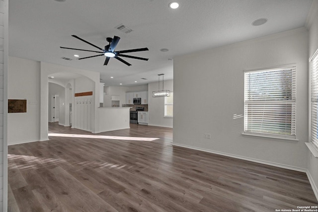 unfurnished living room with baseboards, visible vents, arched walkways, dark wood-style flooring, and ceiling fan