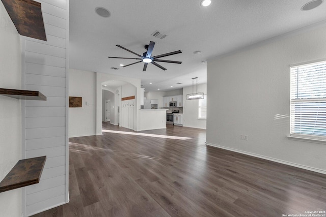 unfurnished living room featuring visible vents, arched walkways, baseboards, ceiling fan, and dark wood-style flooring