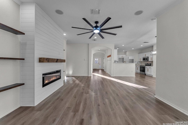 unfurnished living room featuring wood finished floors, arched walkways, visible vents, and a large fireplace