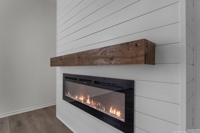 room details featuring a textured wall, wood finished floors, baseboards, and a warm lit fireplace