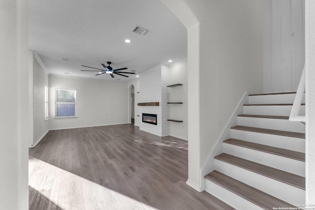 unfurnished living room with wood finished floors, visible vents, a fireplace, ceiling fan, and stairs