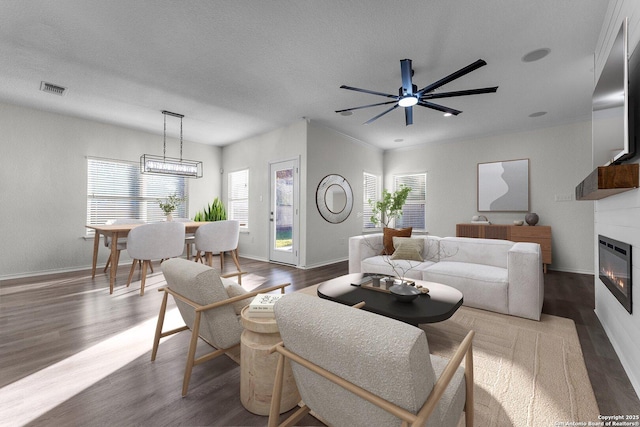 living area with wood finished floors, visible vents, baseboards, a textured ceiling, and a glass covered fireplace