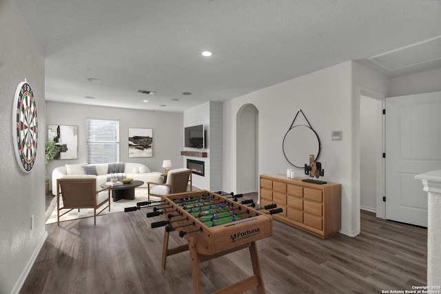 game room with visible vents, baseboards, wood finished floors, a glass covered fireplace, and a textured ceiling